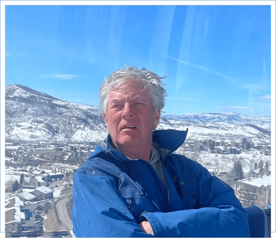 Man with arms crossed overlooking a snowy mountain landscape.