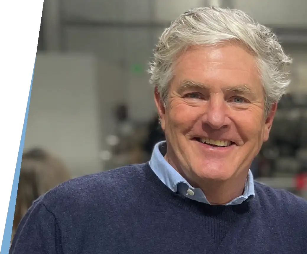 Smiling man with gray hair wearing a blue sweater and collared shirt.
