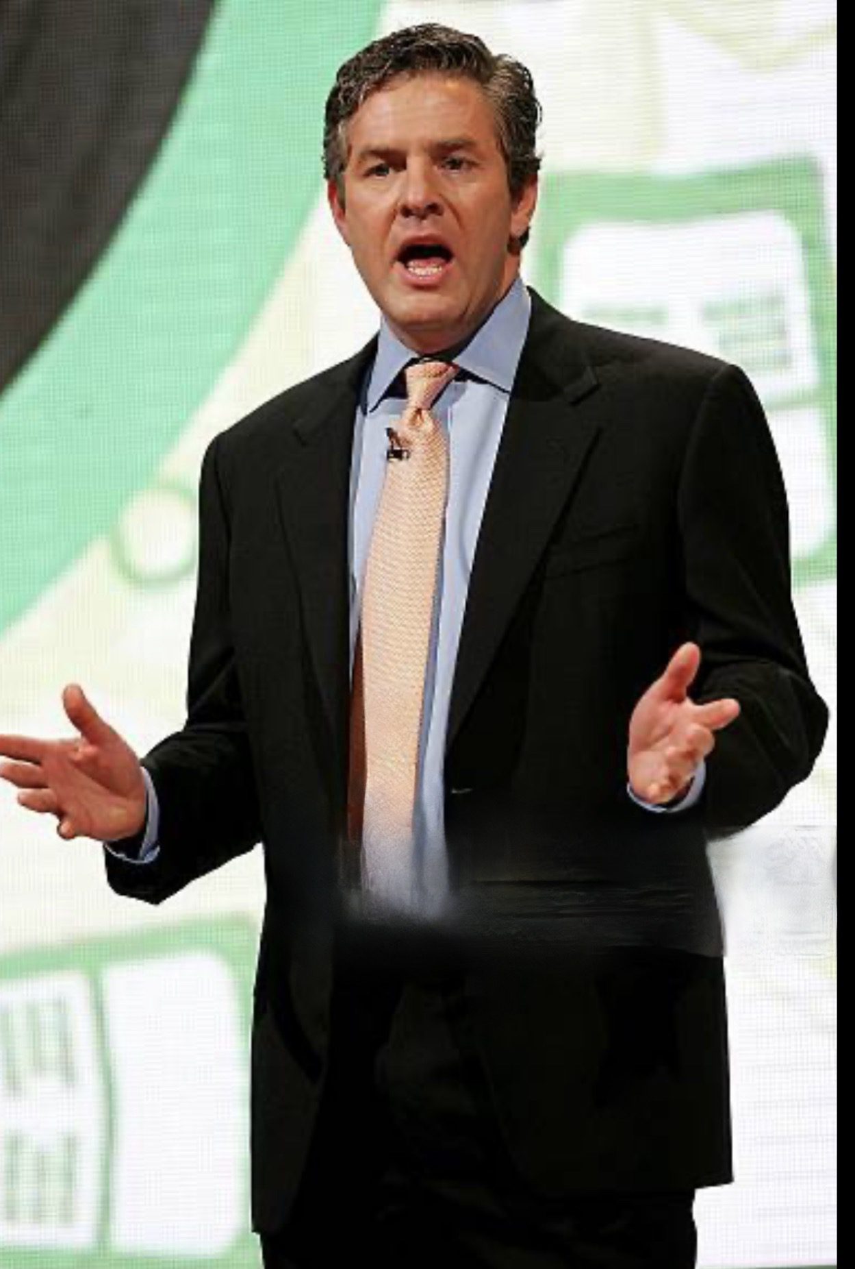 Man in suit speaking with expressive hand gestures on stage.